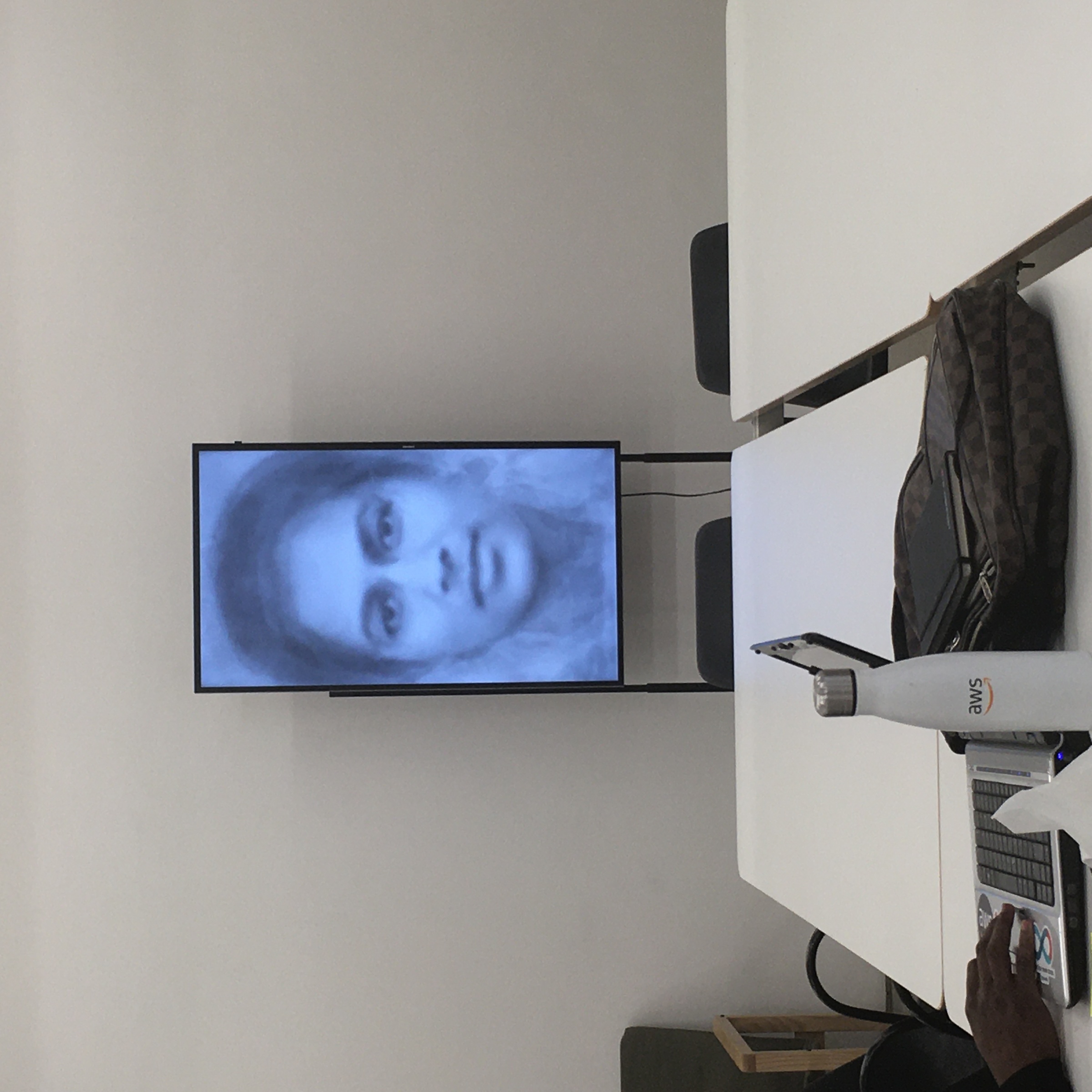 Event photograph from the ‘Informal Interface’ event in A4’s Library. At the front, a white table surrounded by chairs. At the back, Alana Blignaut’s video work ‘Desire for the Public’ plays on a screen.
