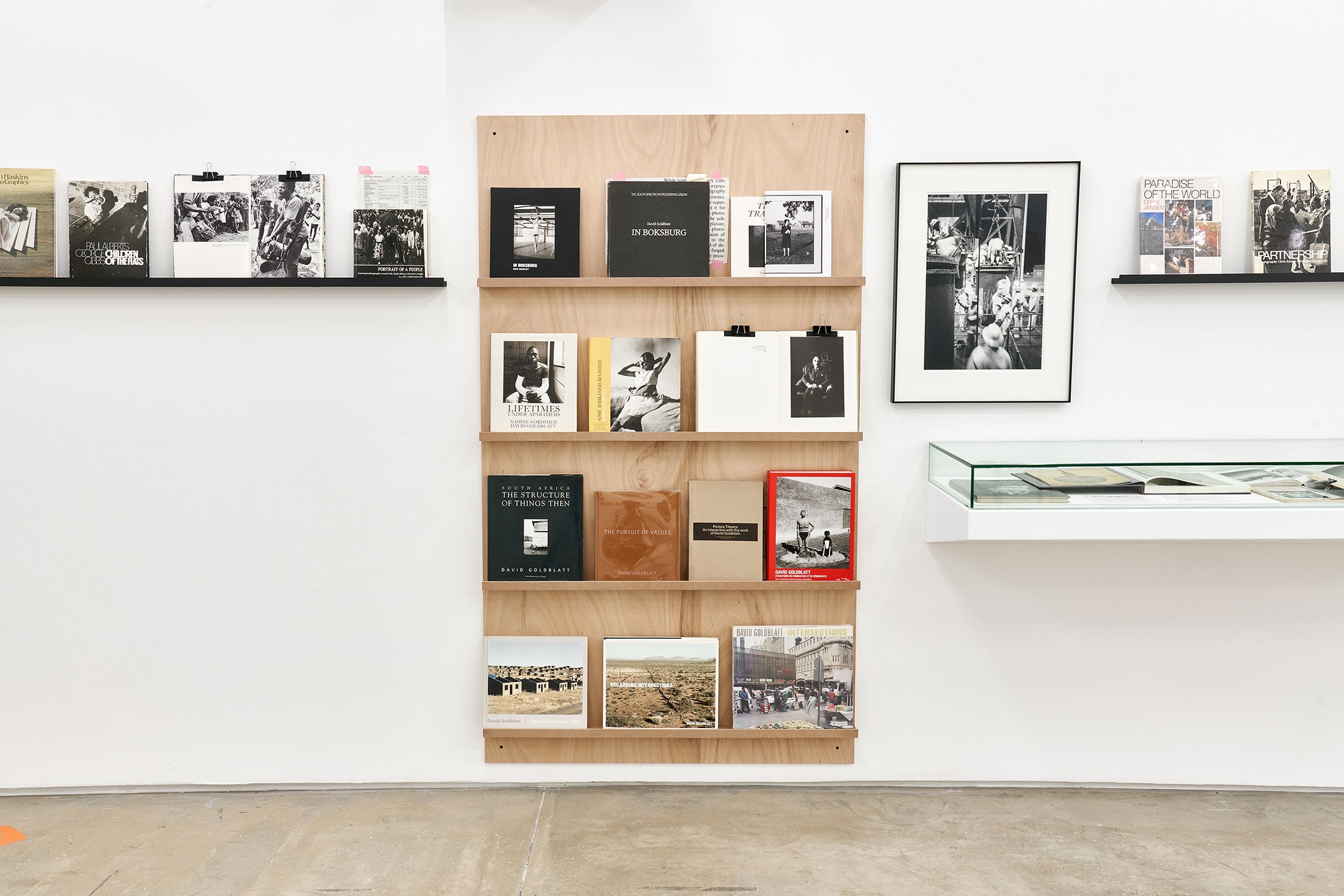 Installation photograph from the Photo Book! Photo-Book! Photobook! exhibition in A4’s Gallery. On the right, David Goldblatt’s photograph ‘Climbing into kibbles at the shaft-head, the shift gets ready to go down. President Steyn No.4 shaft, Welkom, Orange Free State. 1969’ is mounted on the wall above a display shelf in an area dedicated to photobooks from the years 1967 to 1994.
