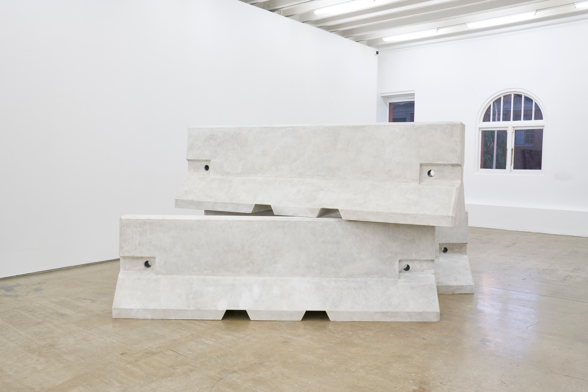 Artwork photograph from the ‘without a clear discernible image’ exhibition in A4’s Gallery. In the middle, Kevin Beasley’s untitled plywood and paint sculpture sits on the gallery floor, resembling concrete road barriers.
