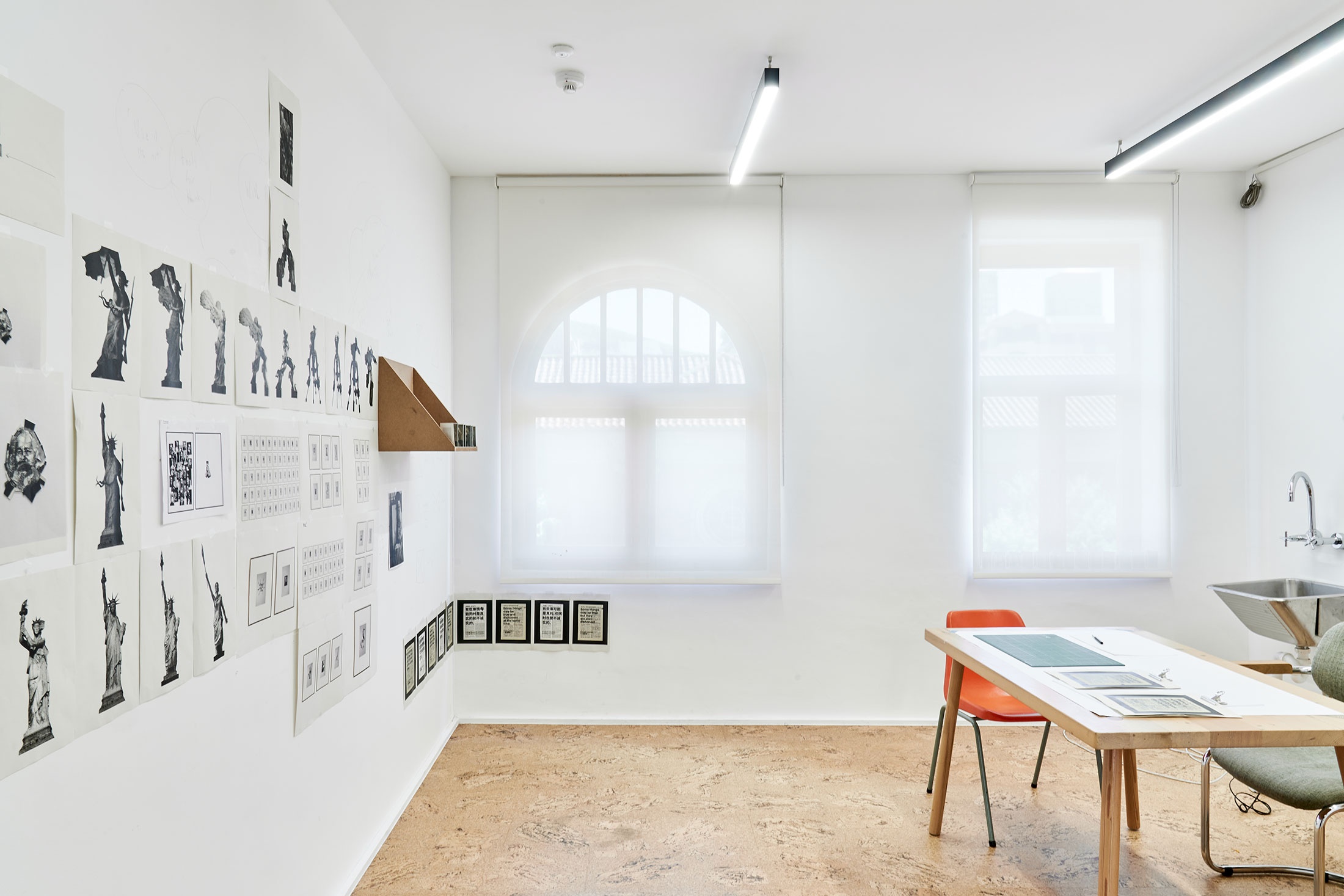 Process photograph from Patrick Waterhouse's 2022 residency in A4 Arts Foundation's studio. On the left, photographic prints on paper are arranged along the studio wall, and on a wooden wall-mounted shelf. On the right, photographic prints are arranged on a table, along with a cutting mat.

